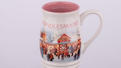 Eine cremeweiße Keramiktasse mit rosa Innenseite zeigt ein buntes Motiv des Nürnberger Christkindlesmarktes und trägt den Schriftzug „Christkindlesmarkt“ sowie die Frage „Mogsd nou an...?“ am inneren Rand.