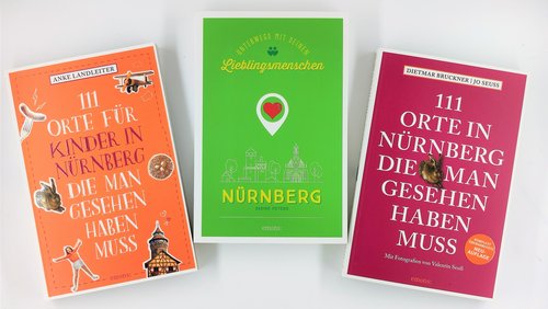 Drei Reiseführer über Nürnberg liegen nebeneinander auf einer weißen Oberfläche: links ein orangefarbenes Buch für Kinder, in der Mitte ein grünes Buch mit dem Titel „Unterwegs mit Deinen Lieblingsmenschen“ und rechts ein pinkfarbenes Buch mit dem Titel „111 Orte in Nürnberg die man gesehen haben muss“.